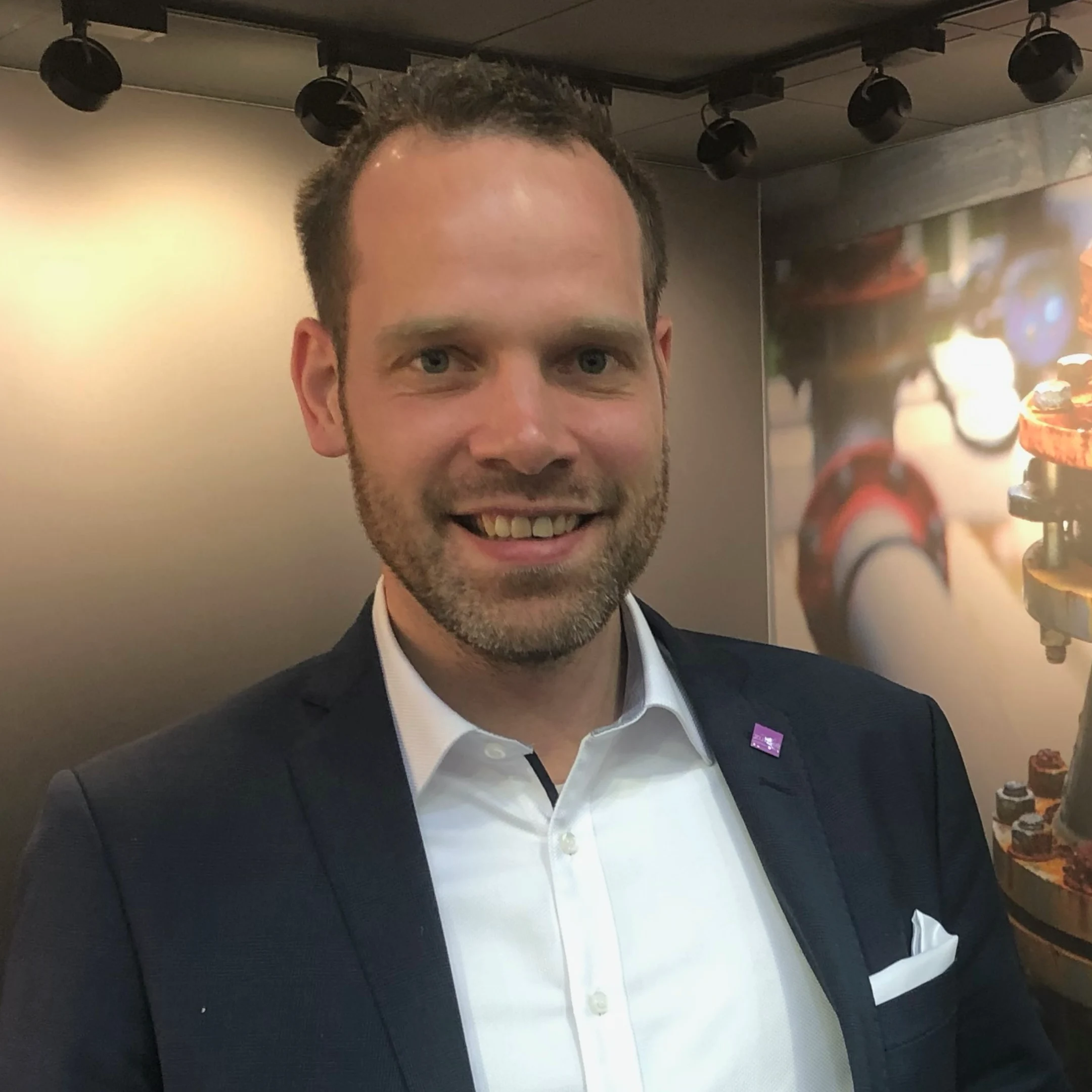 Das Bild zeigt Dennis Ahrens mit weißem Hemd, dunklem Sakko und freundlich in die Kamera lächelnd.