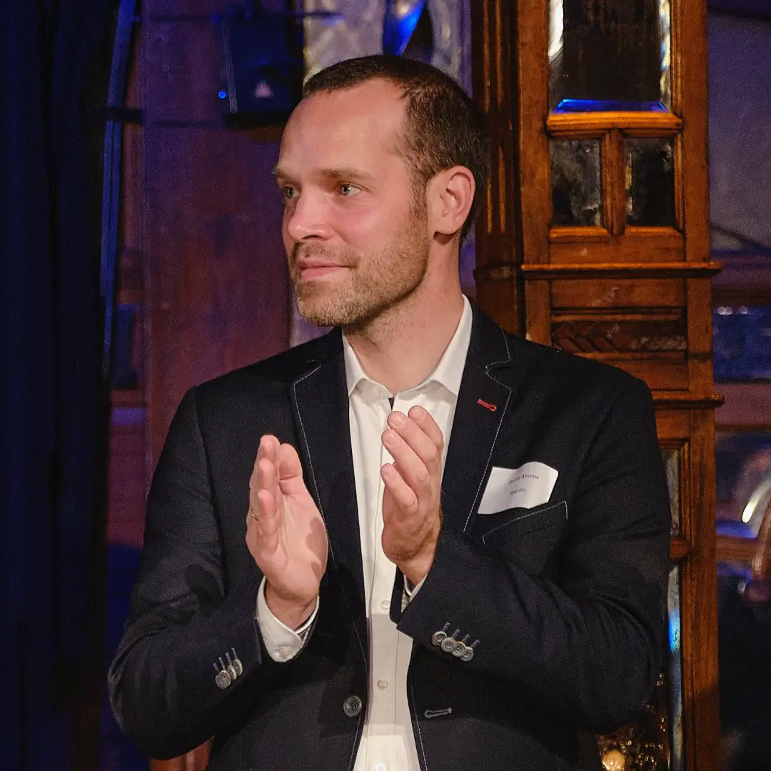 Das Bild zeigt Dennis Ahrens applaudierend auf einem Podium.