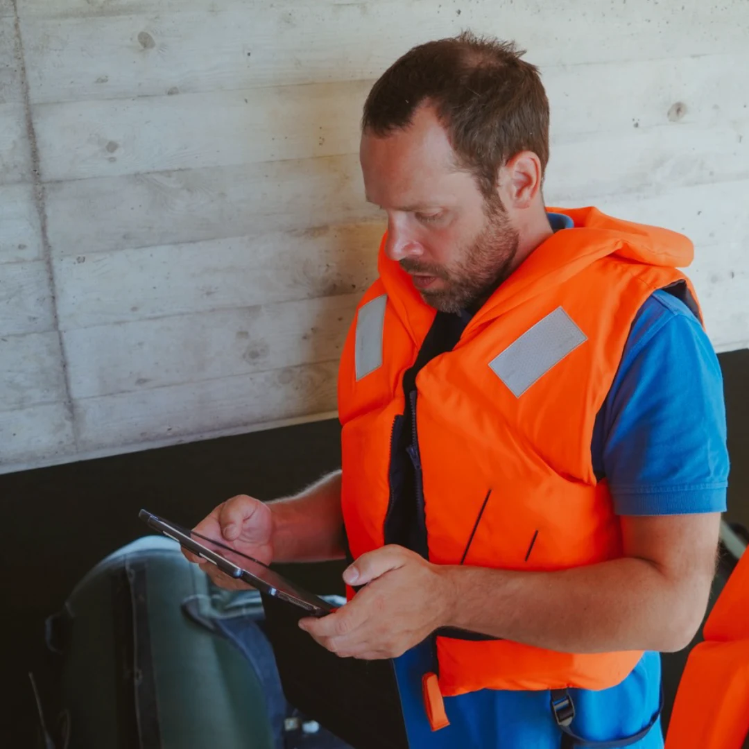 Das Bild zeigt Dennis Ahrens in einer orangefarbenen Warnweste mit einem Tablet in den Händen.