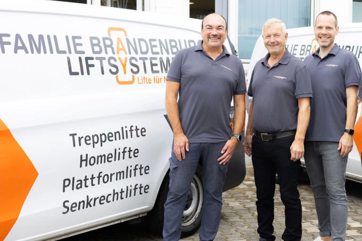 Das Bild zeigt Fahrzeuge der Firma Brandenburg-Liftsysteme. Davor stehen drei Menschen und schauen freundlich in die Kamera.